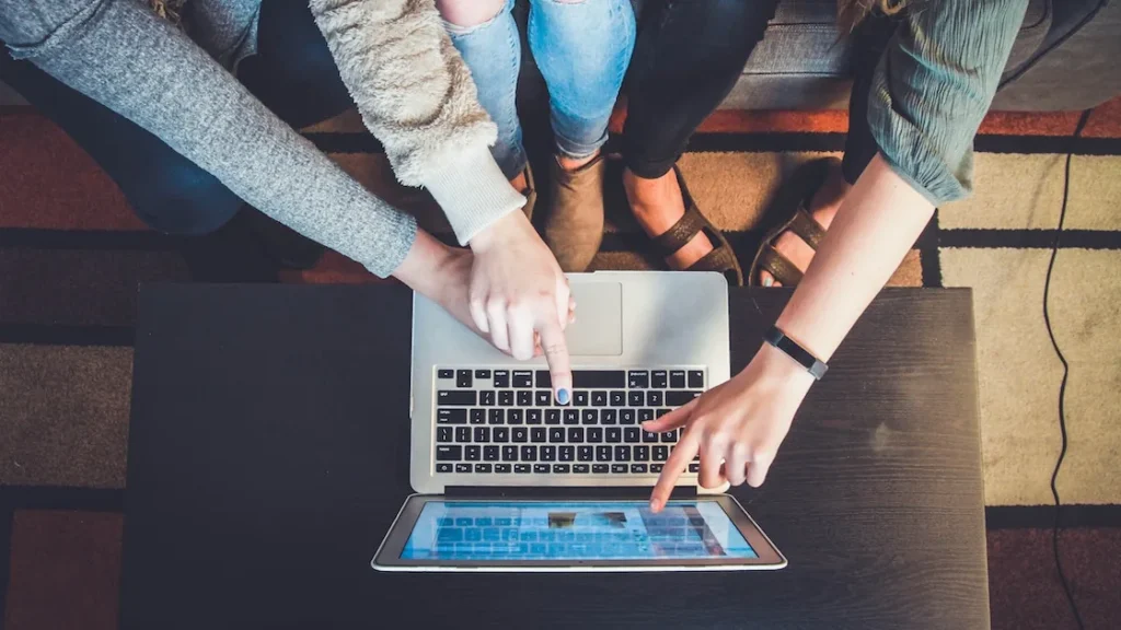 Drei Personen sitzen um einen Laptop und zeigen auf den Bildschirm, während sie gemeinsam online surfen.
